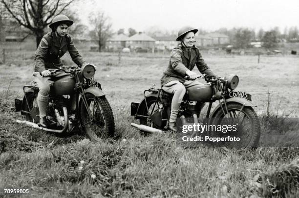 Two female members of the Auxiliary Territorial Service ride Royal Enfield motorcycles over rough ground on an exercise in England during World War...