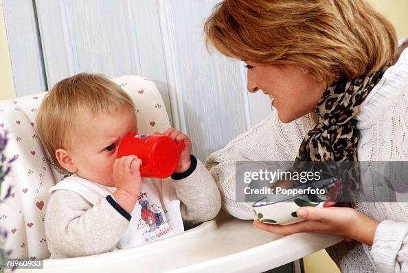 Stock Photography. Attentive mother watches her baby as he sits in a high chair drinking from a training cup. Stock Photography. Attentive mother watches her baby as he sits in a high chair drinking from a training cup.