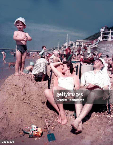 Bournemouth, England A couple relaxing on deck chairs as they enjoy the summer sun on the beach at Bournemouth as a small child stands on top of a...