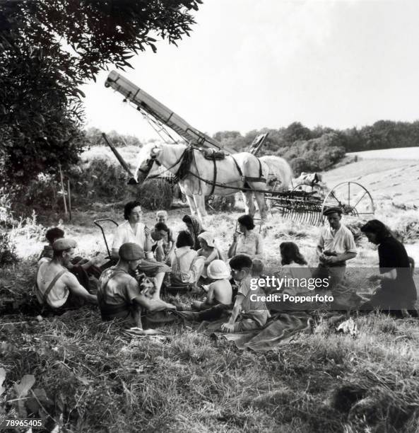 Agriculture, England A large family group sit in the shade of a tree enjoying lunch while taking a break from working on the harvest