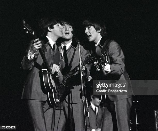 The Beatles 1964 US Tour, L-R: Paul McCartney, John Lennon and George Harrison share a microphone as they sing a song in concert at Carnegie Hall in...