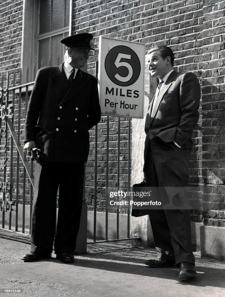1955. English comedy actor Benny Hill talking with a commissionaire ouside Ealing Studios, London.