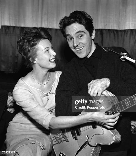 British singer Anthony Newley, holding his guitar, as he sits with Anne Aubrey, 1960