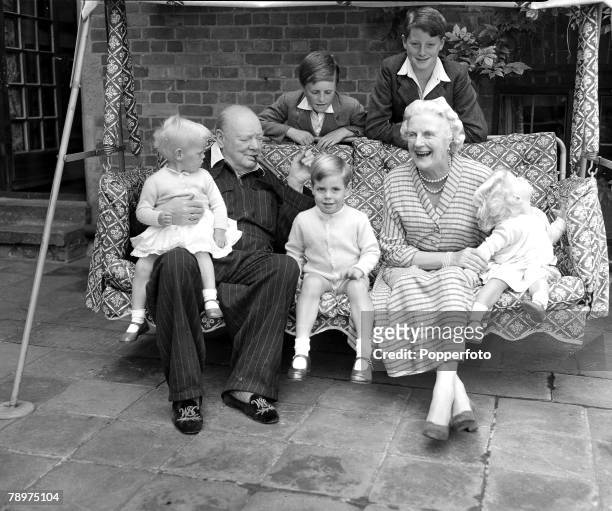 Circa 1951, Mr, Winston Churchill seated outside holds Emma Soames on his knee with young Winston Churchill is standing behind the garden seat and...