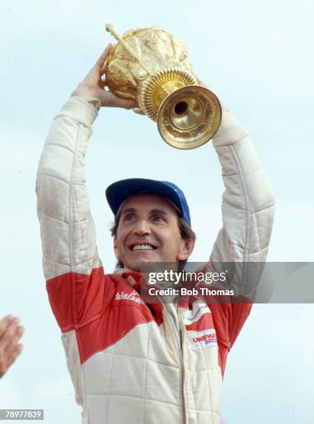 British racing driver John Watson, driver of the Marlboro McLaren International McLaren MP4 Ford Cosworth DFV 3.0 V8, pictured holding the trophy up...