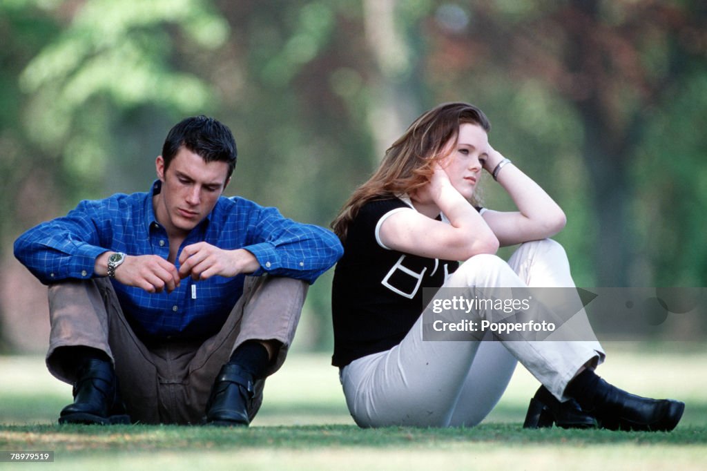 Stock Photography. A young couple in casual dress sitting in the park, the woman appears upset and has back turned on the man.