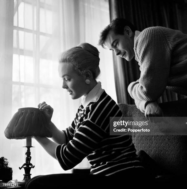 England, British film and movie actress Shirley Eaton adjusts a lamp shade in her house while her fiancee Colin Lenton-Rowe watches her