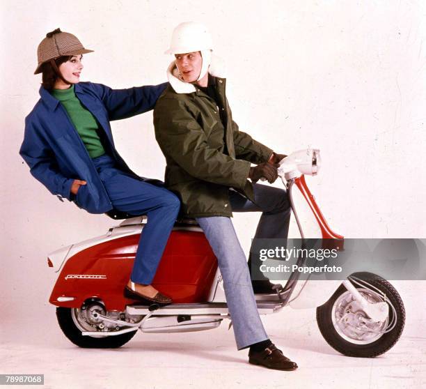 Two young people sitting on a Lambretta scooter wearing suitable fashionable clothing and stylish helmets, the man is looking back at the woman who...