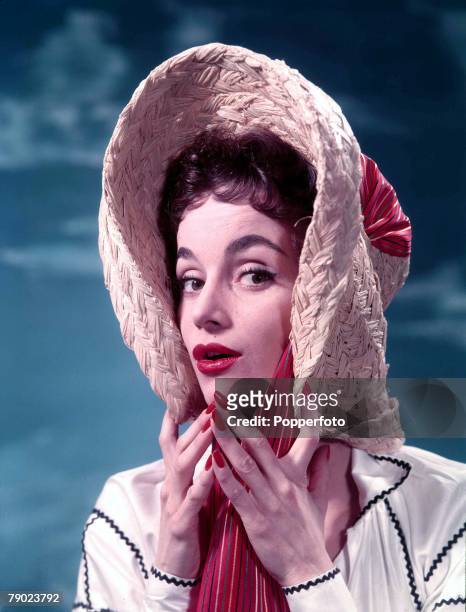 Studio image of a woman with red lipstick and nail polish wearing a Bo Peep style Easter Bonnet, as she poses for the camera, circa 1960.