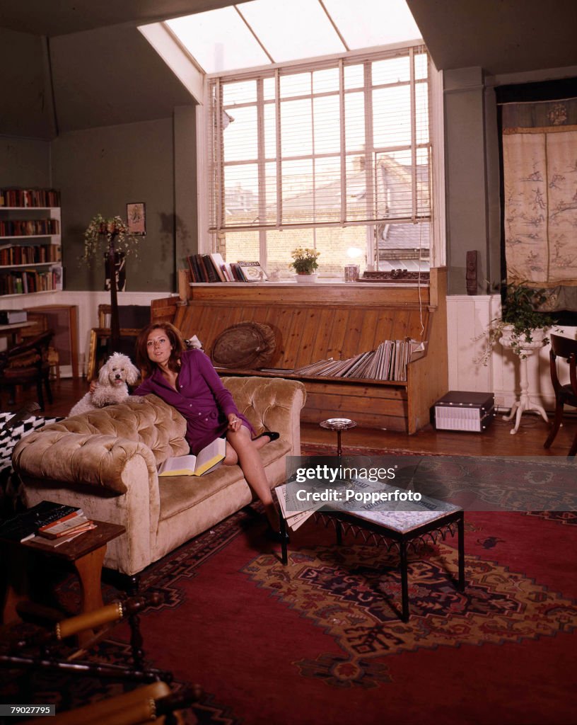 1967. A picture of British actress Diana Rigg, relaxing on a settee in her lounge with one of her pet poodles.