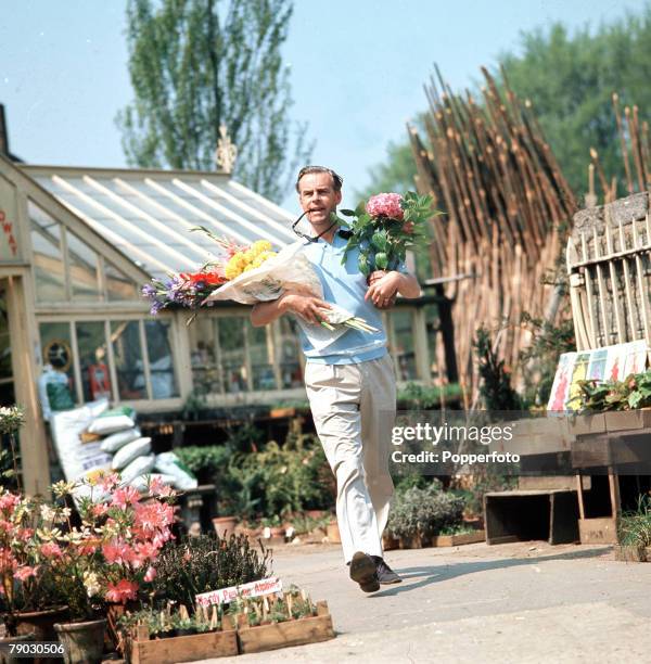 Picture of the British actor Ian Carmichael walking in a garden centre holding some flowers