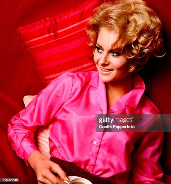 Young blonde haired woman wearing a bright pink blouse as she holds a cup of coffee