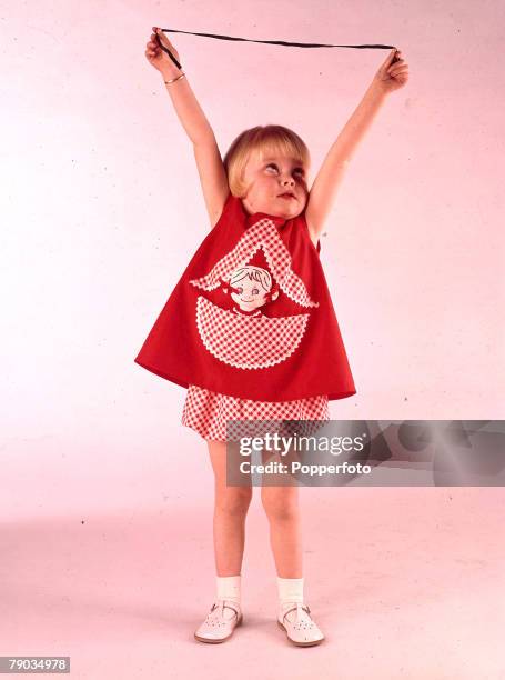 19th April 1964, A picture of a small young girl wearing fashionable red clothing whilst she has her arms out stretched above her head holding a...