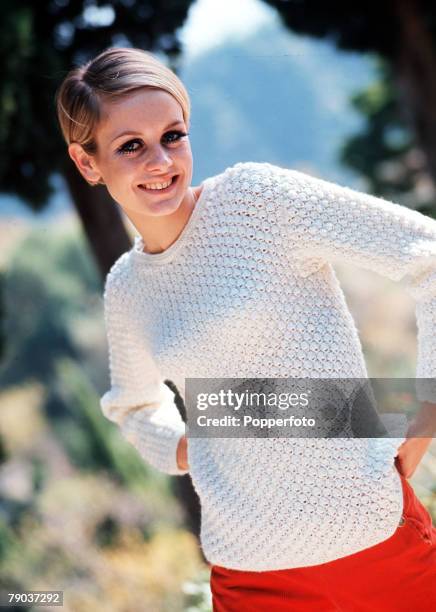 Female fashion model Twiggy wears an interestingly patterned cream coloured long sleeved sweater over a bright red skirt, circa 1965.