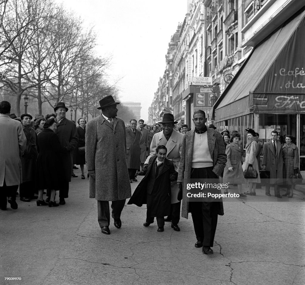 Sport. Boxing 1950. Paris, France. American boxer Sugar Ray Robinson, the World Welterweight boxing champion is pictured on the Champs Elysee walking behind his "bodyguard" midget James A.Karoubi, with George Gainsford (left) and Fred Beale (right).