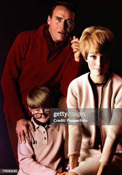 Posed studio image of a man smoking a pipe, wearing a red knitted sweater and a cravat posing for a family portrait with a young frowning boy and a...