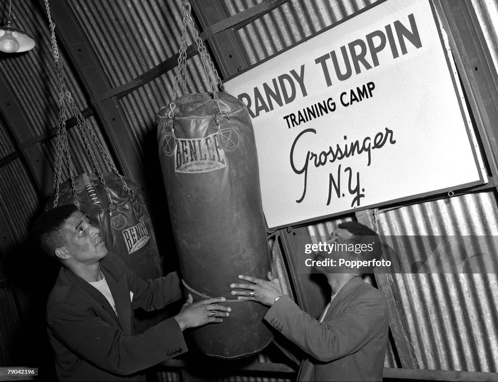 Boxing. 1953. Grossinger, New York, USA. British boxer Randolph "Randy" Turpin is pictured in the plane hanger which he uses as a gym, fixing a punchbag with his brother Jackie.
