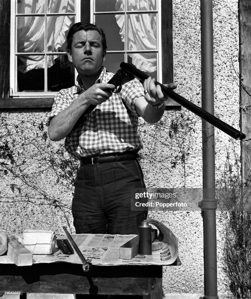 England. 1955. British actor Kenneth More is pictured cleaning his shotgun at his country home.