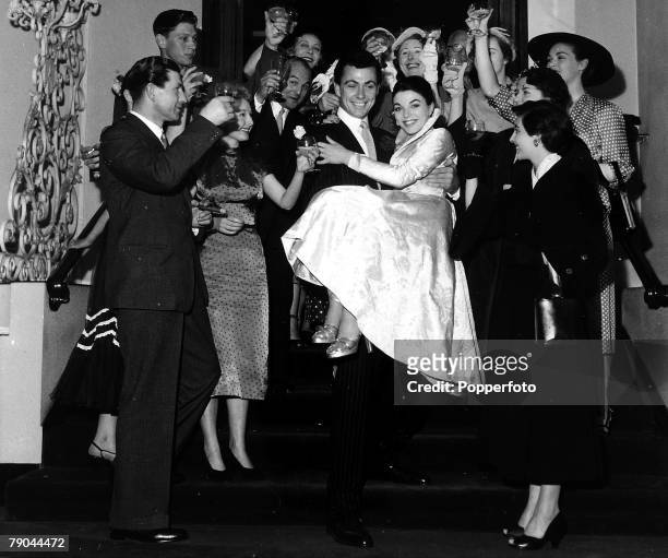 London, England, 25th May 1952, British Actor Maxwell Reed carries his new bride, actress Joan Collins down the stairs surrounded by guests after...