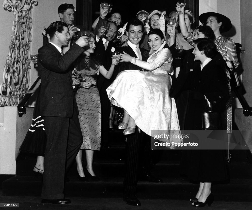 London, England. 25th May 1952. British Actor Maxwell Reed carries his new bride, actress Joan Collins down the stairs surrounded by guests after their wedding.