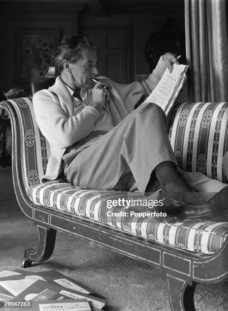 Welsh actor, composer and songwriter Ivor Novello relaxes on his chaise longue while making a few last minute adjustments to the score of a song from...