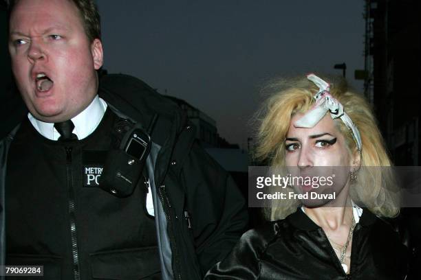 Singer Amy Winehouse walks down the street with a police escort from a North London shop as a crowd has gathered outside on January 17, 2008 in...