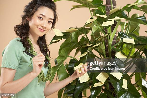 green' businesswoman sticking post-it notes on a leafy office plant - chinese collar stockfoto's en -beelden