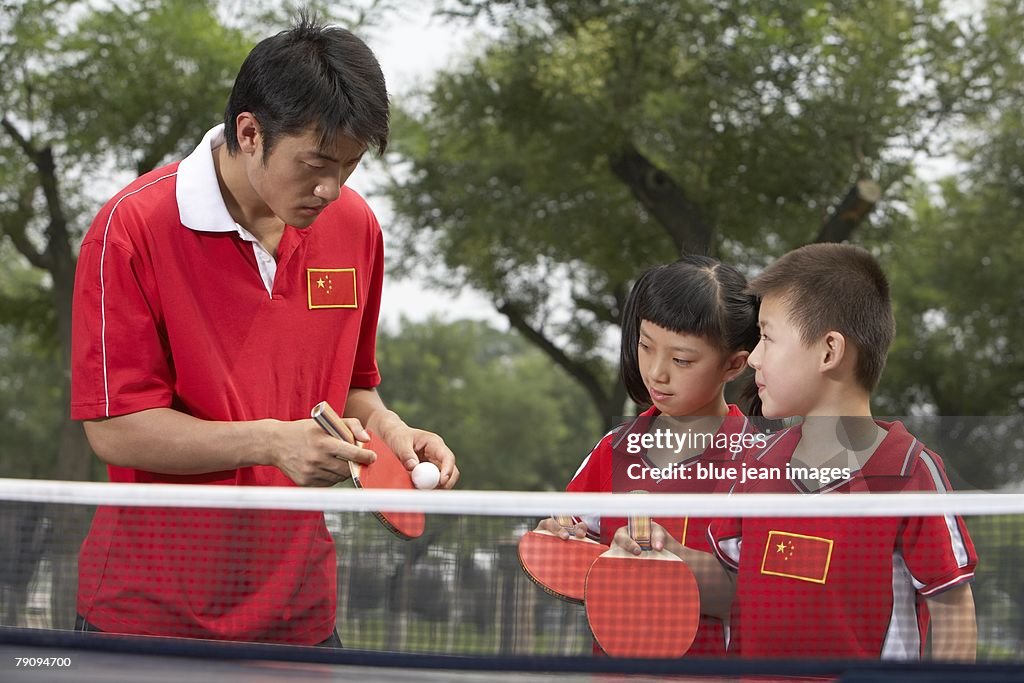 The next generation. An athlete coaching two children in table tennis.