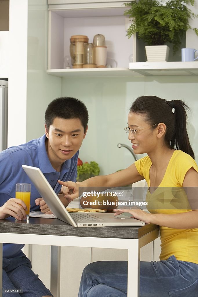 A young couple surf the internet at the kitchen table.