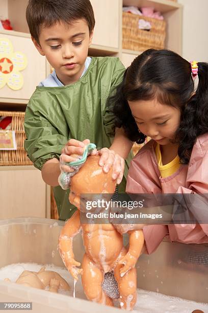 two children giving their dolls baths at kindergarten. - chinese dolls stock pictures, royalty-free photos & images
