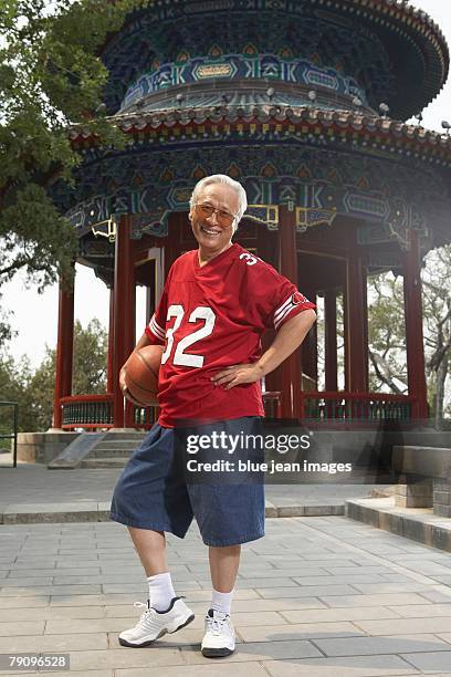 a older man dressed in a football jersey and holding a basketball is having fun. - basketball jersey stock pictures, royalty-free photos & images