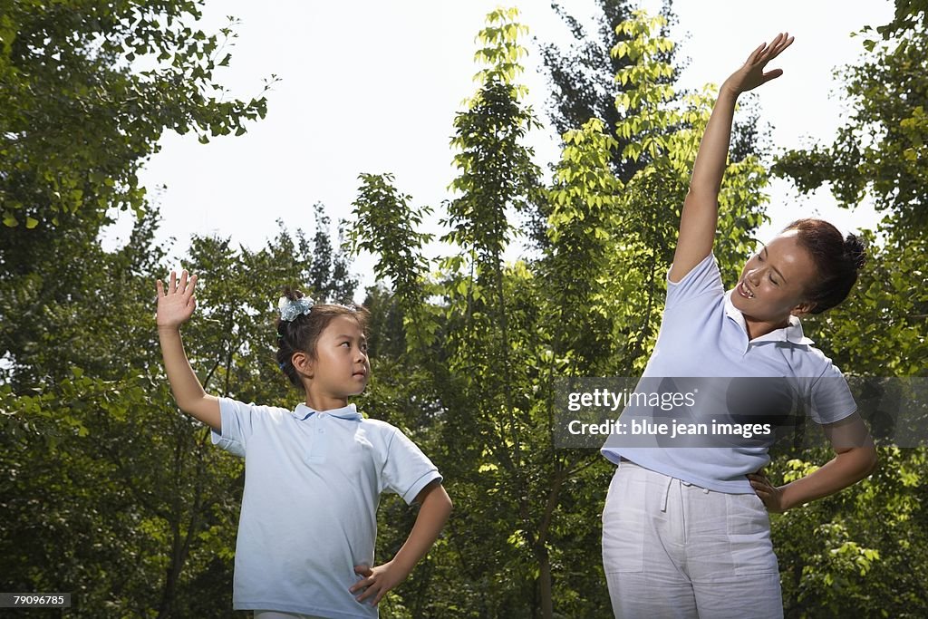 A mother and daughter stretching in a clearing.