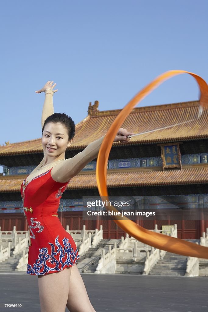 A rhythmic gymnastics athlete practices in front of an ancient, Ming Dynasty-style Chinese temple square, early morning.