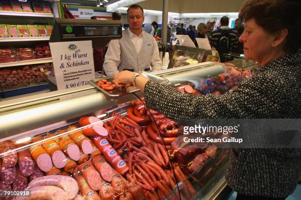 Visitor samples dried sausage as different types of traditional German sausage, ham, salami and other meat products lie on display at a butcher's...