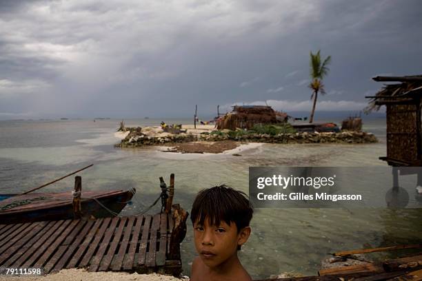 Young Kuna Indian stands on a pier on the small island of Corbisky, pop. 200, in front of a tiny island which is home to a Kuna family, in El...