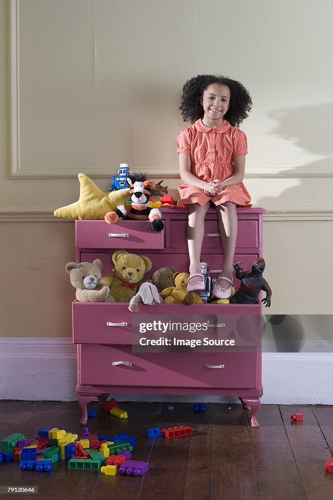Girl sitting on dresser of toys