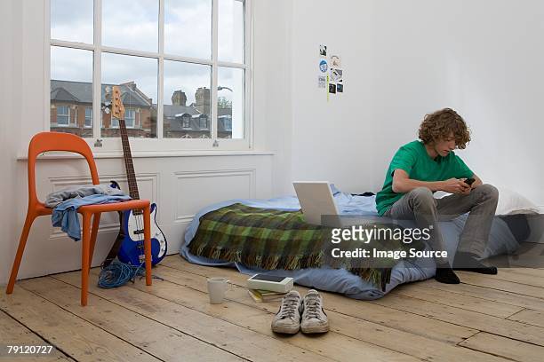 teenage boy using cell phone - boy sitting on bed stock-fotos und bilder
