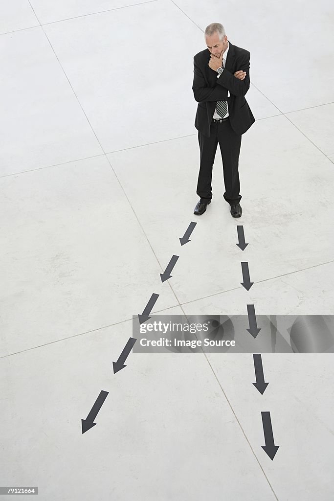 Businessman looking at arrows on floor