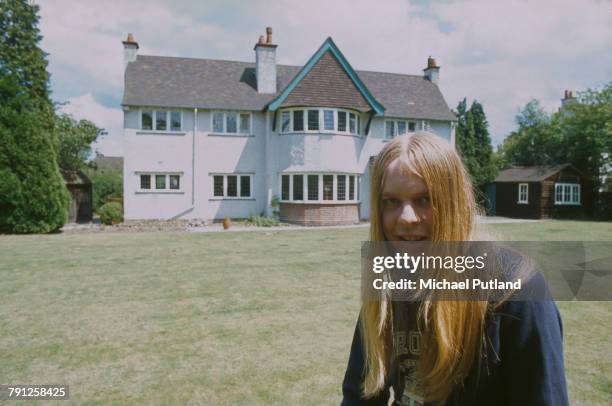 English composer and keyboard player Rick Wakeman pictured wearing a Brown University sweatshirt as he stands in a garden in England circa 1973.