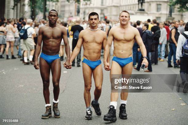 Three men wearing small blue swimming trunks taking part in the London Pride march, 1st July 2000.