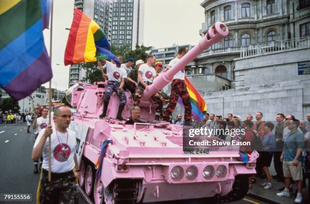 Men in camouflage trousers riding a pink tank and carrying rainbow flags during the Lesbian and Gay Pride event, London, 24th June 1995. The tank is...