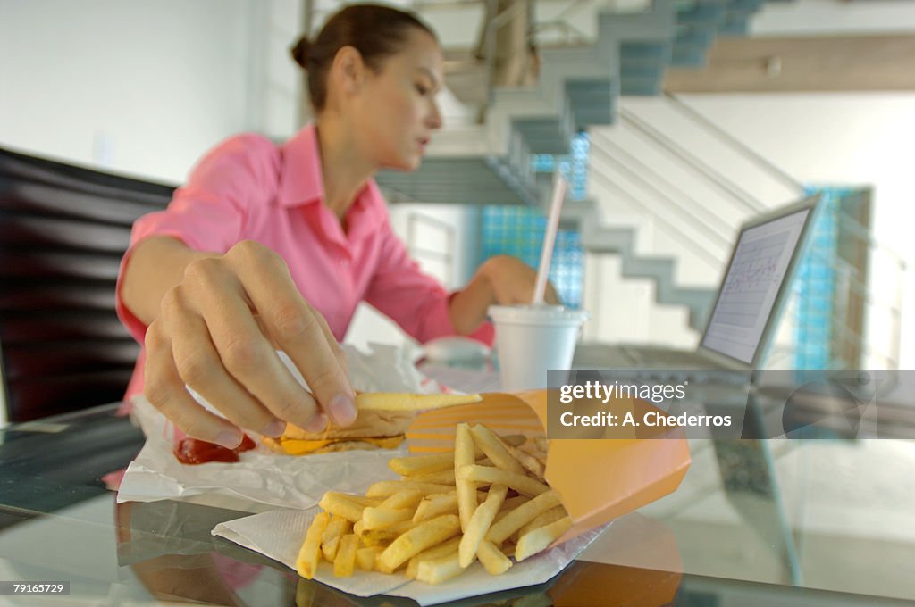 Businesswoman eating French fries, using laptop