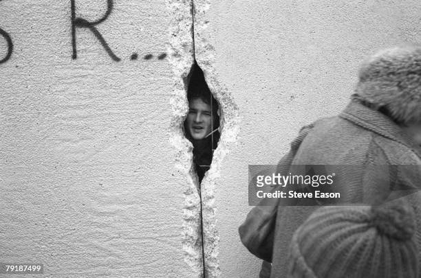 Young man peers into East Berlin though a hole in the Berlin Wall at the effective end of the city's partition, 31st December 1989.