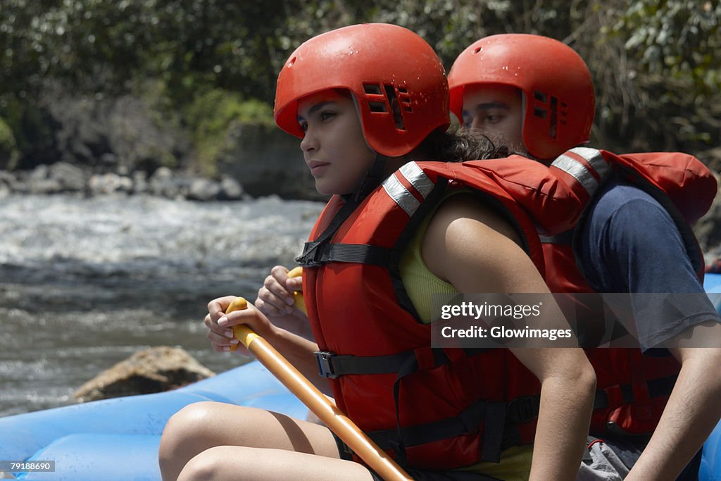 Side profile of a young man and a young woman rafting in a river