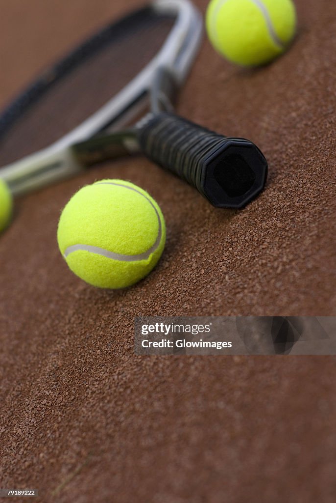 Close-up of three tennis balls and a racket in a court