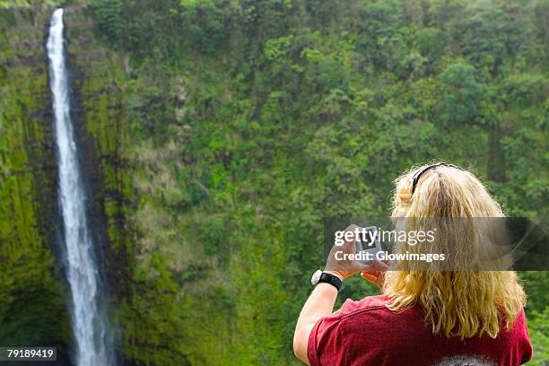 rear view of a woman taking a photograph of a waterfall, akaka falls, akaka falls state park, hilo, big island, hawaii islands, usa - akaka state falls park stock pictures, royalty-free photos & images