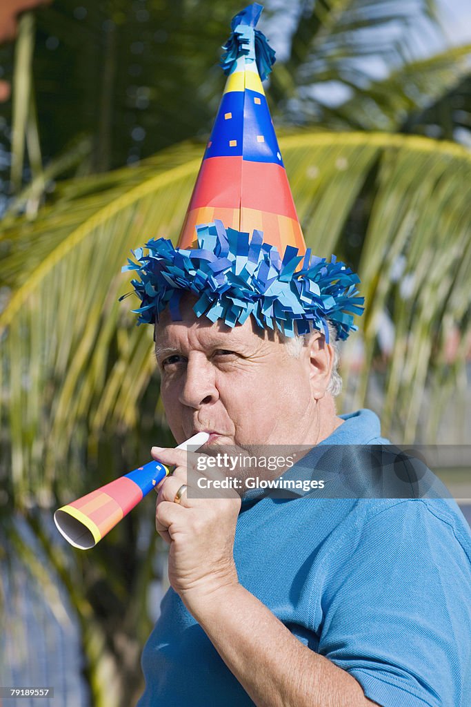 Side profile of a senior man blowing a party horn blower