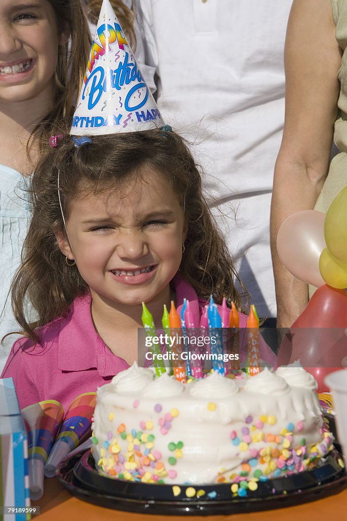 Portrait of a girl with her sisters standing in front of a birthday cake