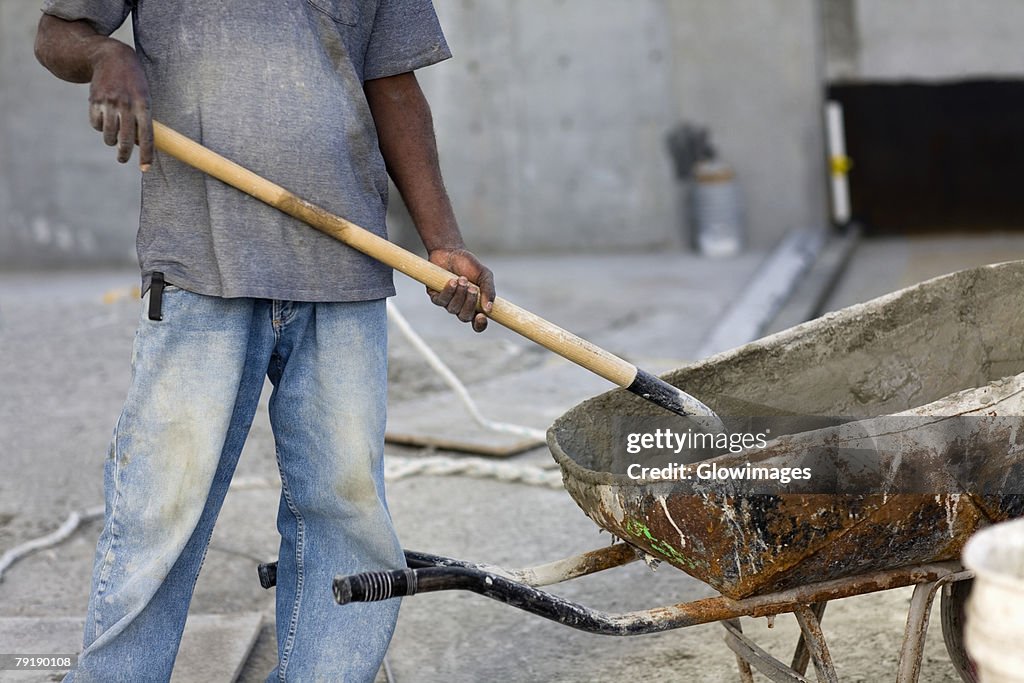 Mid section view of a male construction worker shoveling cement
