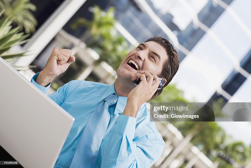 Businessman talking on a mobile phone and raising his fist in front of a laptop